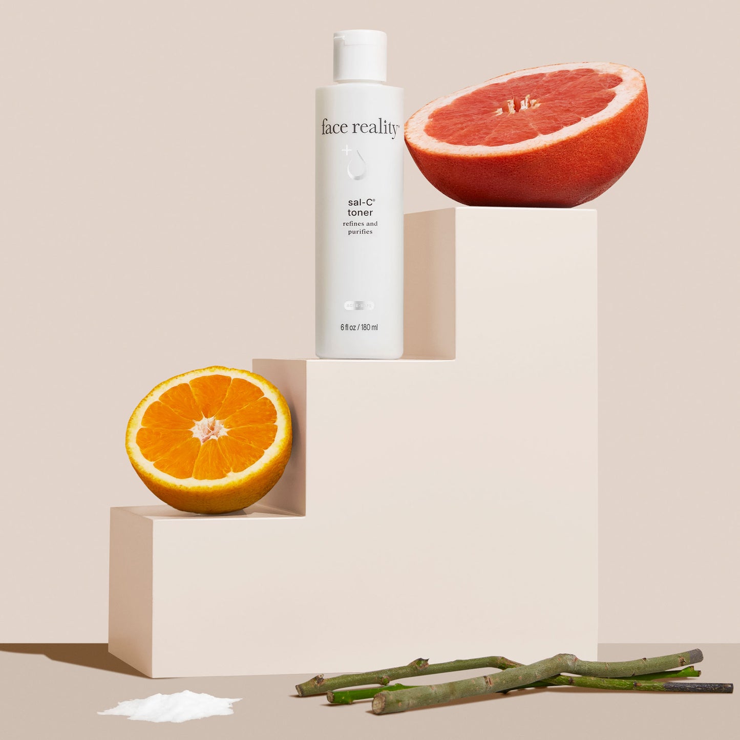 Skincare bottle labeled face reality with a halved orange and grapefruit on a beige background