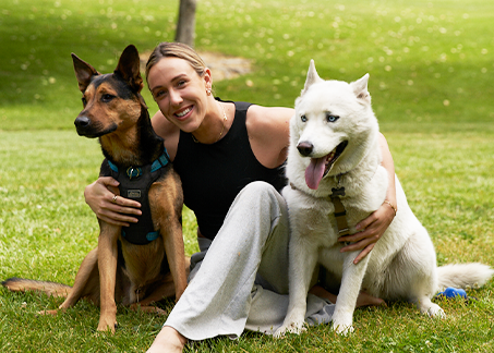 Abbey Weitzeil sitting on a lawn with her dogs, Weylin and Jax.
