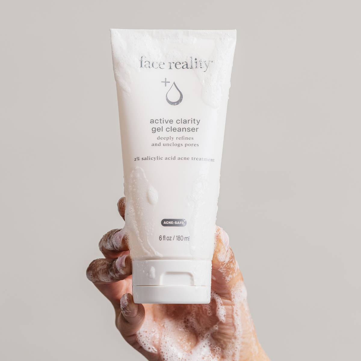 Hand with foaming product holding a tube of active clarity gel cleanser against a light background