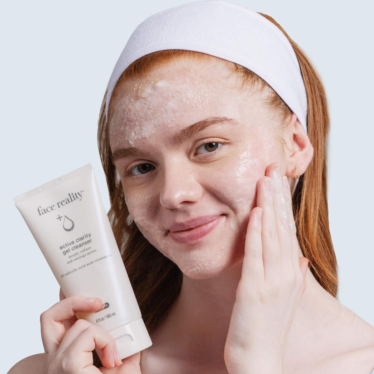 Person applying product and holding a tube of active clarity gel cleanser against a white background