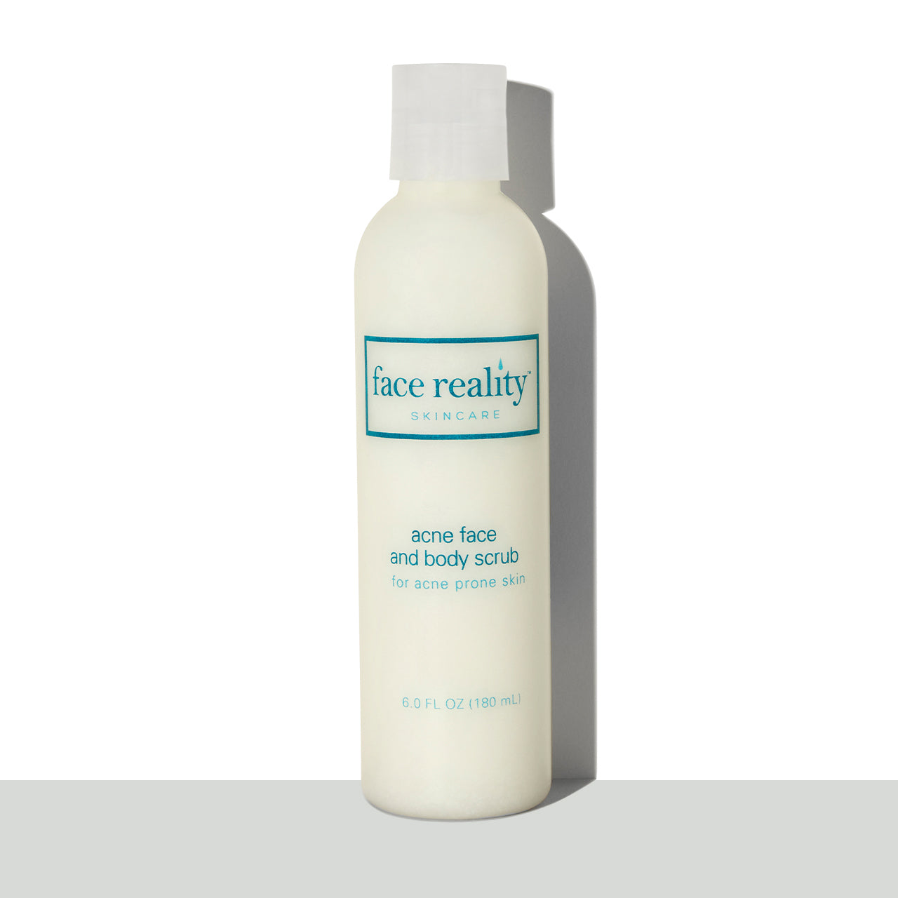 Clear six ounce bottle of Face Reality acne face and body scrub in front of a white background on a grey surface