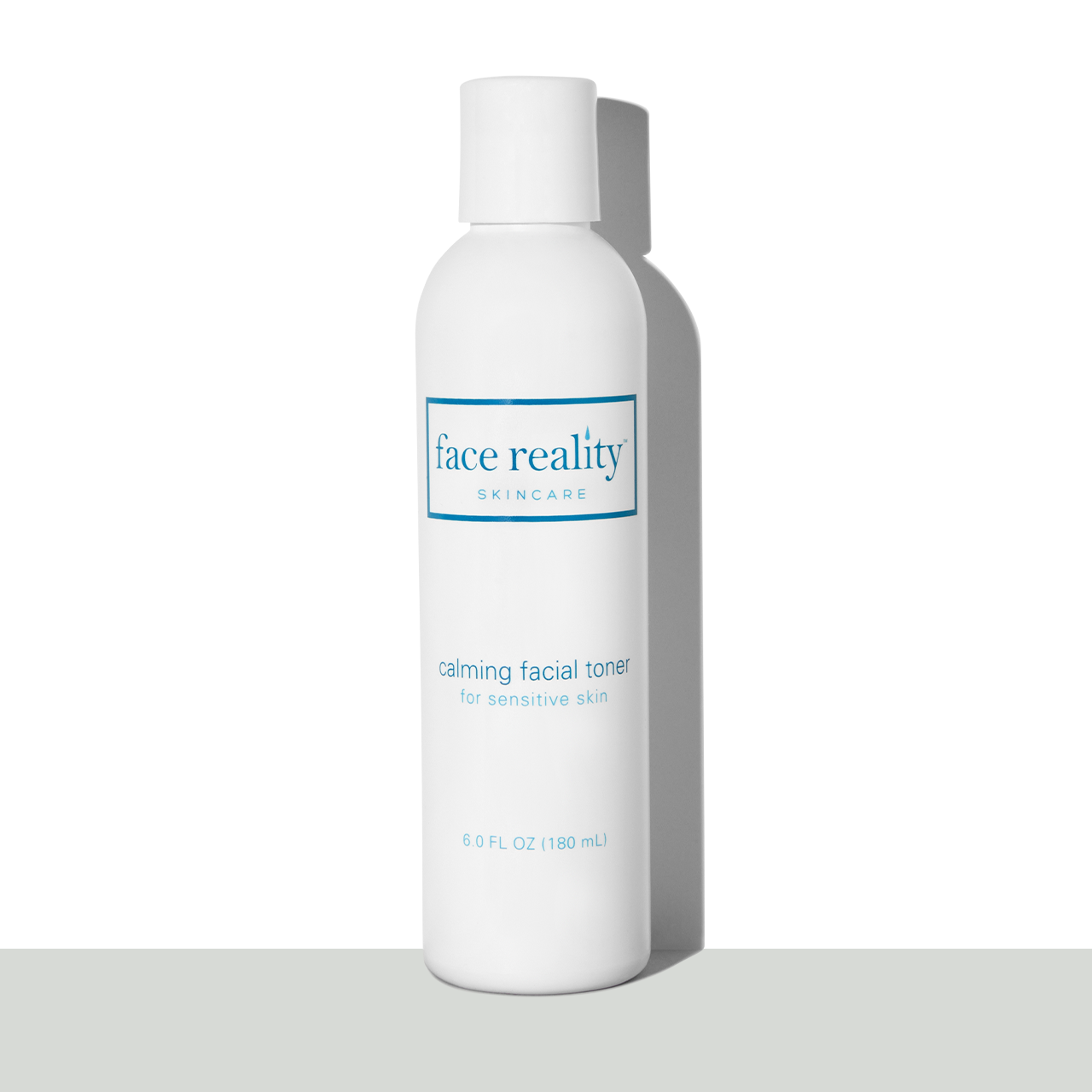 White six ounce bottle of Face Reality Calming Facial Toner in front of a white background on a grey surface